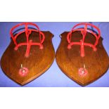 A pair of red painted tack racks, mounted on shield-shaped wooden plaques