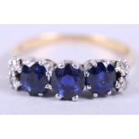 A yellow metal dress ring set three sapphires with two diamonds to each shoulder, size N