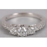 A three stone diamond ring set four diamond accents to each shoulder in white metal mount, stamped