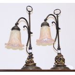 A pair of Art Nouveau style bronzed table lamps with pink glass shades (one damaged)
