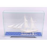 A white metal filigree model of a sailing boat, in glass case