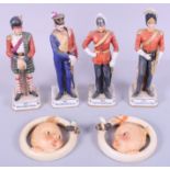 Three porcelain figures of soldiers and two Hummel baby's head wall plaques