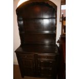 An oak dresser with arch top and open plate shelves over two drawers and cupboards, on stile