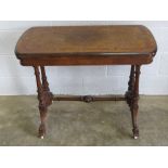 A fine walnut fold over games table raised over shaped supports upon an H shaped base terminating