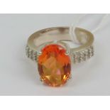 A silver cocktail ring having large oval faceted orange stone and white stone encrusted shoulders,
