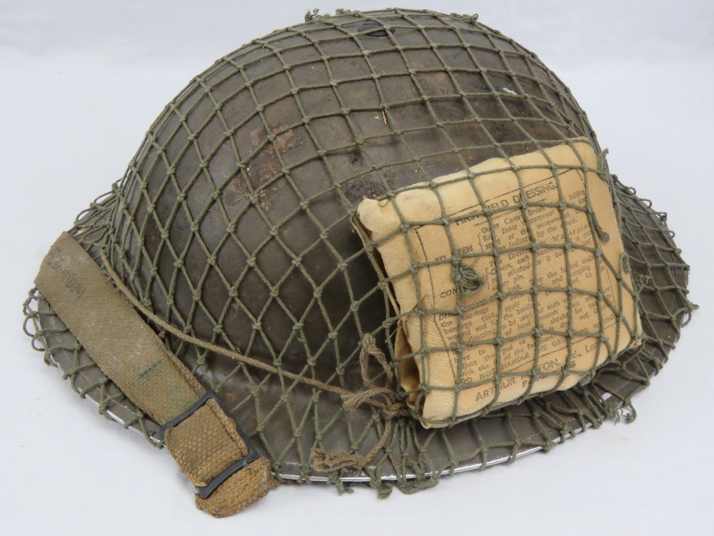 A WWII British Military 'Tommy' helmet with camo netting and emergency first aid field dressing