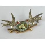 A vintage brooch in the form of two birds watching over three faux pearl 'eggs' in a nest upon a