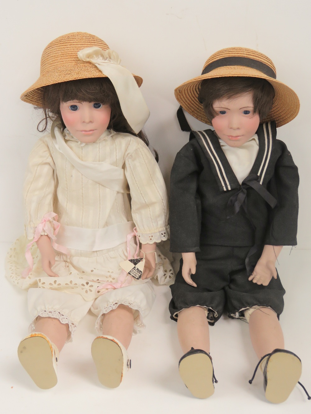 A pair of contemporary porcelain dolls each having glass eyes and vintage attire,