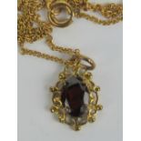 An oval cut garnet pendant on yellow metal filigree setting with 9ct gold fine link chain,