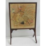 A vintage fire screen having embroidery of a cockerel and hen on cream silk ground behind glazed