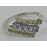 A silver cocktail ring set with three rows of lilac oval cut and white square cut stones,