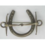 A white metal brooch or stock pin in the form of a horseshoe and snaffle, 5cm wide.