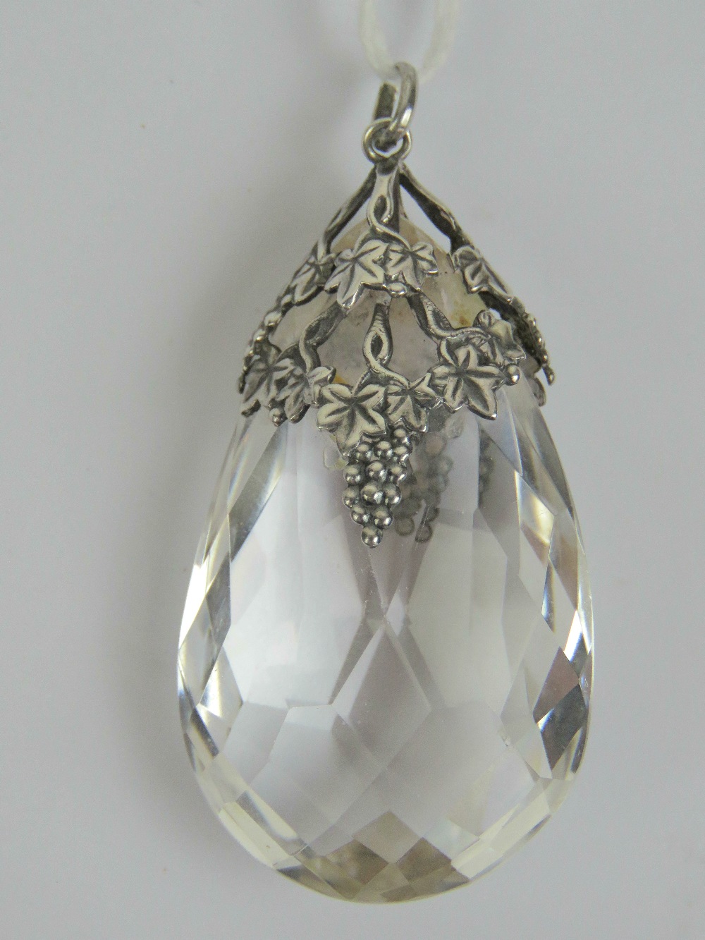 A large teardrop shaped faceted crystal in a pierced grape vine design white metal pendant mount, 5.