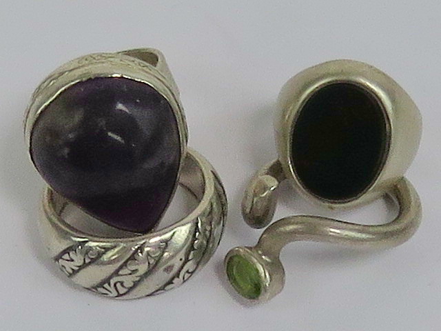 Four white metal rings including a peridot set wrap around ring and a bloodstone signet ring (band