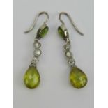 A pair of diamond and peridot earrings each having three graduated round cut brilliant diamonds.