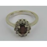 A 14ct white gold ring having central oval garnet surrounded by a gallery of white stones,