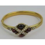 A vintage yellow metal hinged bangle having four garnet cabachons and seed pearls to front, 19.7g.