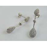 A pair of 18ct white gold pave diamond set earrings having teardrop shaped stud with pendulum bar