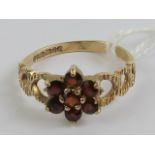 A 9ct gold ring having seven garnet daisy cluster and carved heart pattern to band, hallmarked 375,