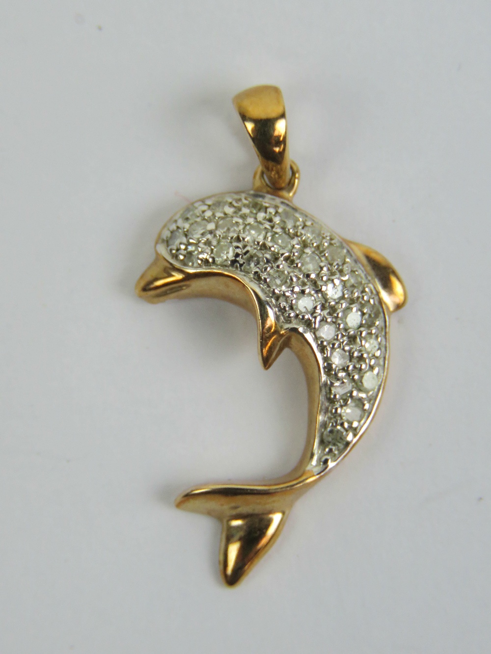 A 9ct gold and diamond dolphin pendant having yellow metal tail and fins,