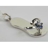 A white gold charm in the form of a flip flop having sapphire and diamond floral cluster to 'strap',