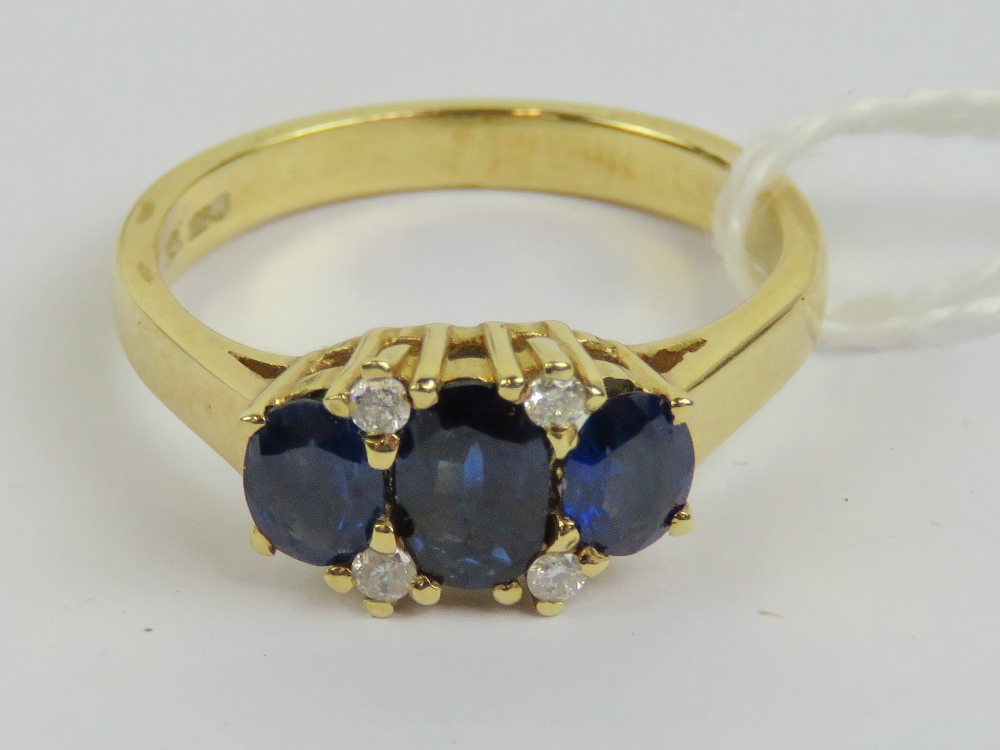 An 18ct gold sapphire and diamond ring having three graduated oval cut sapphires of royal blue hue,