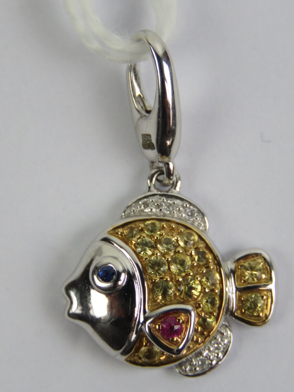 An 18ct white gold charm in the form of a fish having yellow sapphire scales,