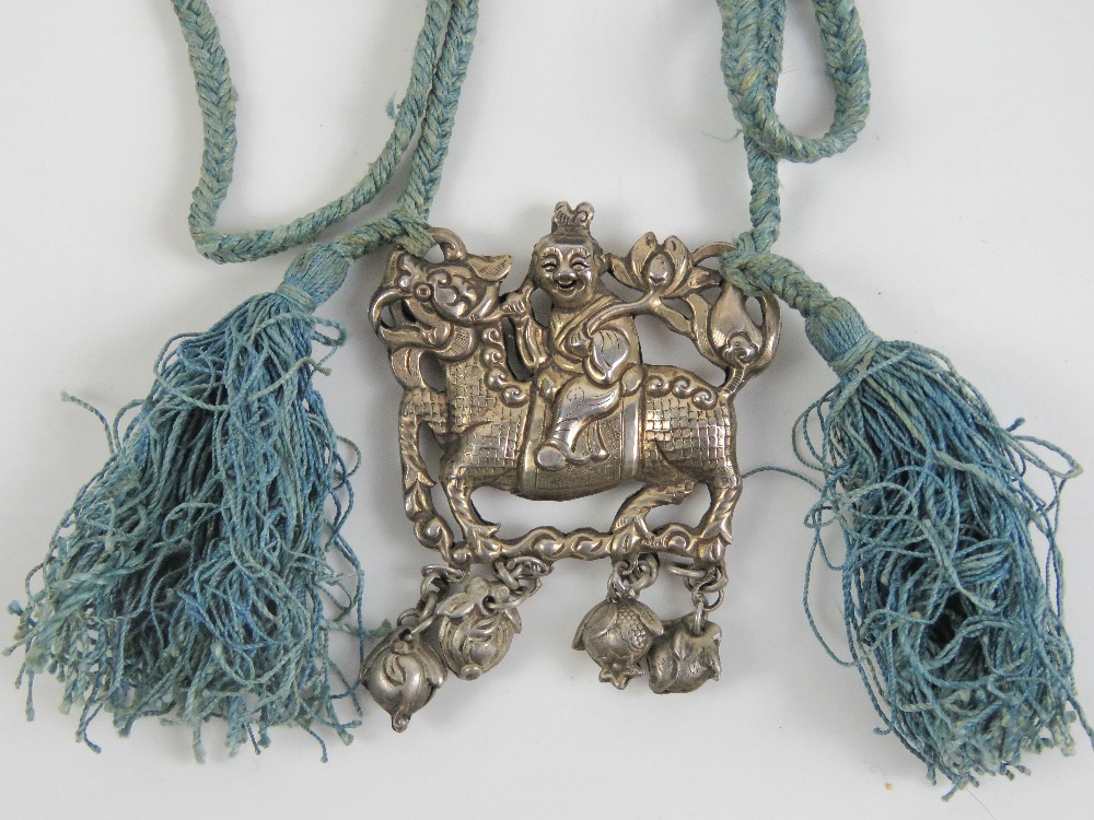 A Chinese white metal two sided pendant in the form of a Qilin (Kirin or Girin) with smiling rider,