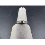 A WHITE METAL DIAMOND RING. THE CENTRAL DIAMOND IS A PRINCESS CUT IN A FOUR CLAW CORNER SETTING WITH