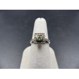 A 14K STAMPED WHITE METAL DIAMOND RING. THE CENTRAL DIAMOND IS PRINCESS CUT IN A RUB OVER SETTING