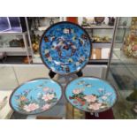 A PAIR OF JAPANESE CLOISONNE DISHES WITH CRANES FLYING IN A BLUE SKY OVER FLOWERS. Dia.30cms