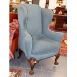 A CARVED WALNUT EARLY GEORGIAN DESIGN WINGBACK ARMCHAIR WITH FEATHER CUSHION ON BALL AND CLAW FEET.