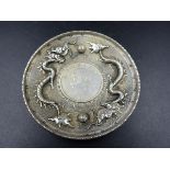 AN ORIENTAL WHITE METAL SAUCER WITH DRAGON DECORATION AND AN INSET CENTRAL MEDALLION WITH VARIOUS