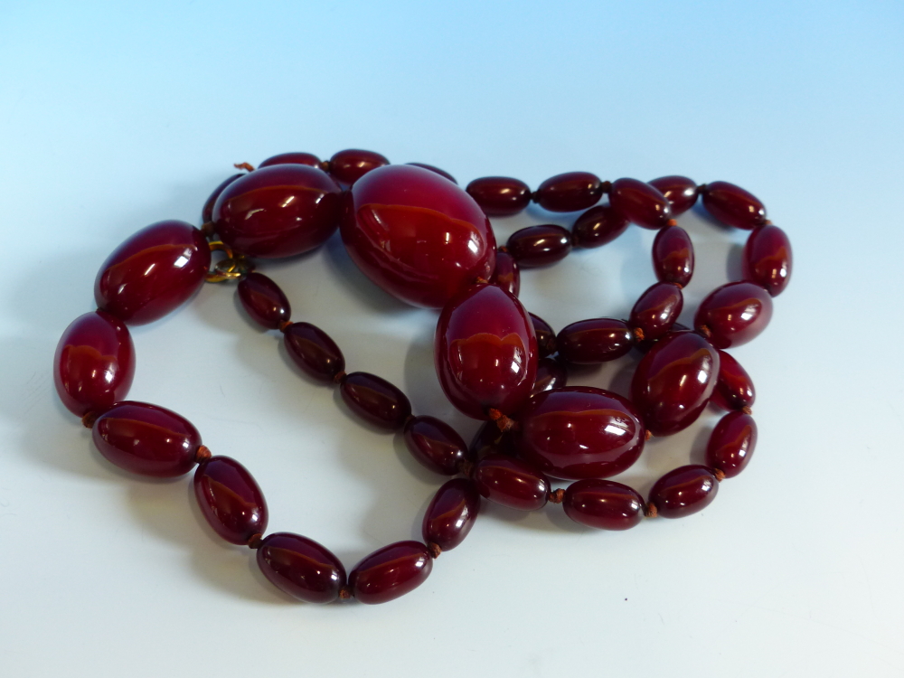A GRADUATED ROW OF CHERRY AMBER BEADS, KNOTTED. LENGTH 76cms, WEIGHT 60 grams.