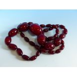 A GRADUATED ROW OF CHERRY AMBER BEADS, KNOTTED. LENGTH 76cms, WEIGHT 60 grams.