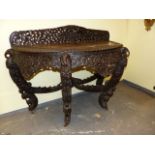 AN INDIAN HARDWOOD DEMI LUNE TABLE EXTENSIVELY CARVED WITH BIRDS, ANIMALS AND FOLIAGE, THE FOUR