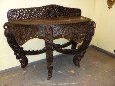 AN INDIAN HARDWOOD DEMI LUNE TABLE EXTENSIVELY CARVED WITH BIRDS, ANIMALS AND FOLIAGE, THE FOUR