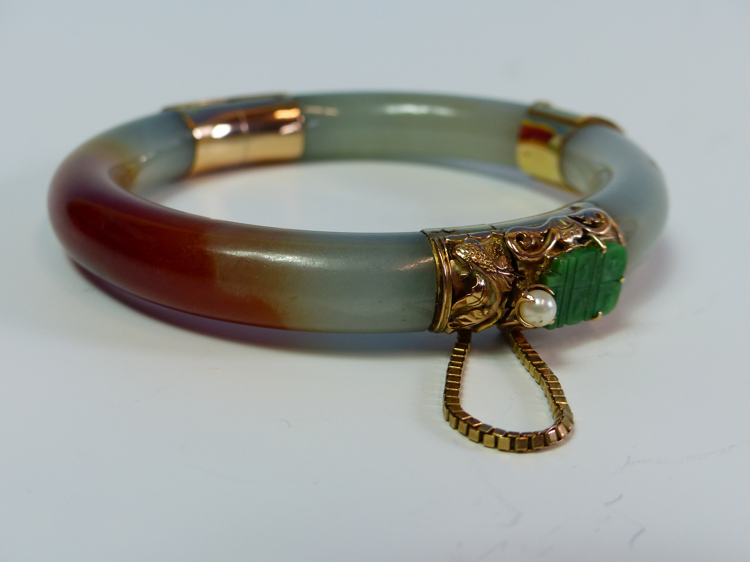 A 14K STAMPED GOLD MOUNTED JADE BANGLE FINISHED WITH A CARVED FISH, JADE AND PEARL CLASP COMPLETE