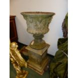 A COMPOSITE STONE CLASSICAL GARDEN URN WITH MASK DECORATED PLINTH BASE. OVERALL H.110cms.