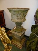 A COMPOSITE STONE CLASSICAL GARDEN URN WITH MASK DECORATED PLINTH BASE. OVERALL H.110cms.