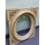 A CREAM COLOURED GLAZED FRAME FOR AN OVAL PICTURE, THE SQUARED SPANDREL BRACKETS WITH FOLIATE