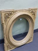 A CREAM COLOURED GLAZED FRAME FOR AN OVAL PICTURE, THE SQUARED SPANDREL BRACKETS WITH FOLIATE