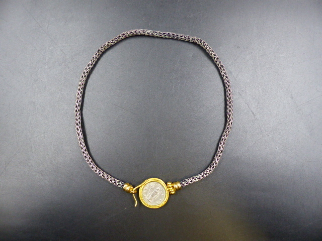 AN EARLY ROMAN COIN MOUNTED AS A PENDANT IN YELLOW METAL ATTACHED TO A WHITE METAL CHAIN.