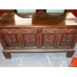 AN OAK COFFER, THE FOUR PANEL FRONT AND FEET CARVED WITH FOLIAGE, THE INTERIOR WITH A CANDLE BOX.