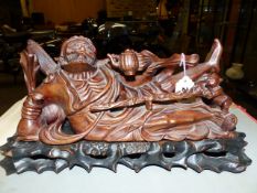 A HARDWOOD CARVING OF LI DIEHGUEI RECLINING AS HE DRINKS FROM A TEAPOT WHILE A CHILD HOLDS HIS