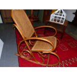 AN ANTIQUE BENTWOOD THONET STYLE ROCKING CHAIR WITH CANE BACK AND SEAT.