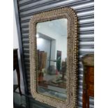 AN INTERESTING LARGE WALL MIRROR, THE FRAME ENCRUSTED WITH COWRIE SHELLS. 70 x 124cms.