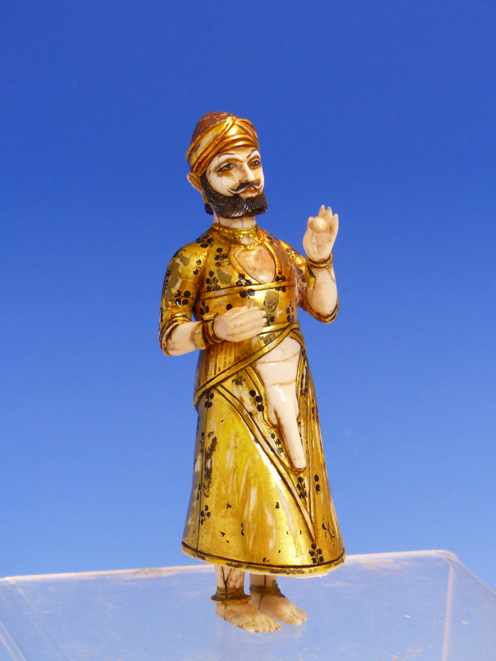 AN ANTIQUE MUGHAL GILT AND PAINTED IVORY FIGURE OF A PARTIALLY CLAD MAN STANDING HOLDING A POD