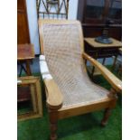 A VINTAGE HARDWOOD PLANTATION CHAIR WITH CANED SEAT AND SWING OUT LEG SUPPORTS.