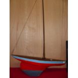 A POND YACHT WITH PLANKED DECK, SINGLE MAST, WEIGHTED KEEL, THE RED HULL TOPPED BY A TURQUOISE BAND.